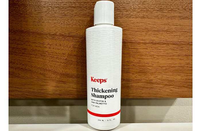 A bottle of Keeps Thickening Shampoo against a wooden background.