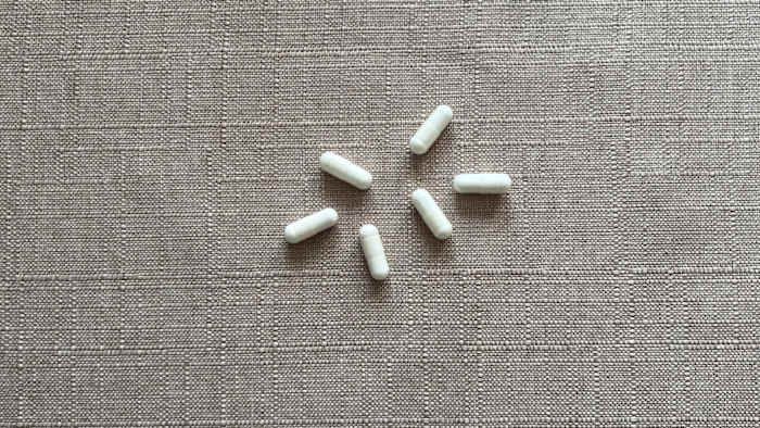 Six nondescript capsules against a neutral background representing the size and shape of common probiotic supplements