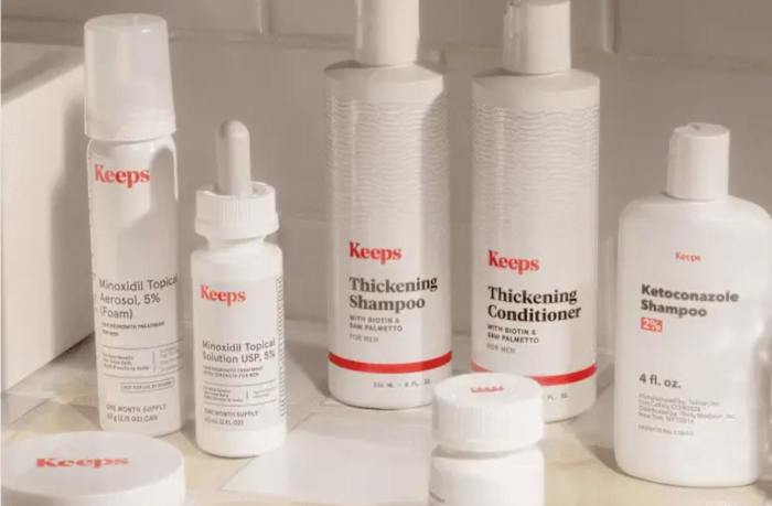 Several bottles of white Keeps hair thickening and hair regrowth products in a white tiled bathroom.