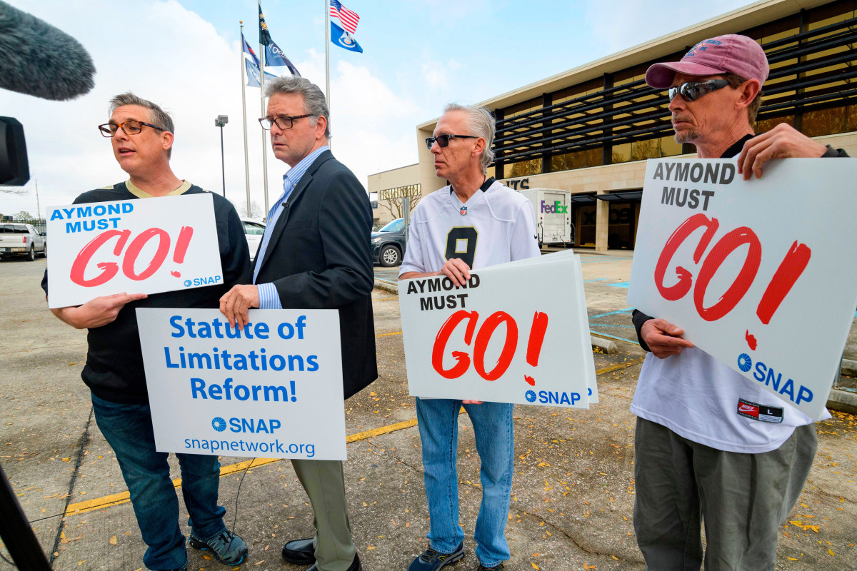 Four men holding signs reading Aymond must go
