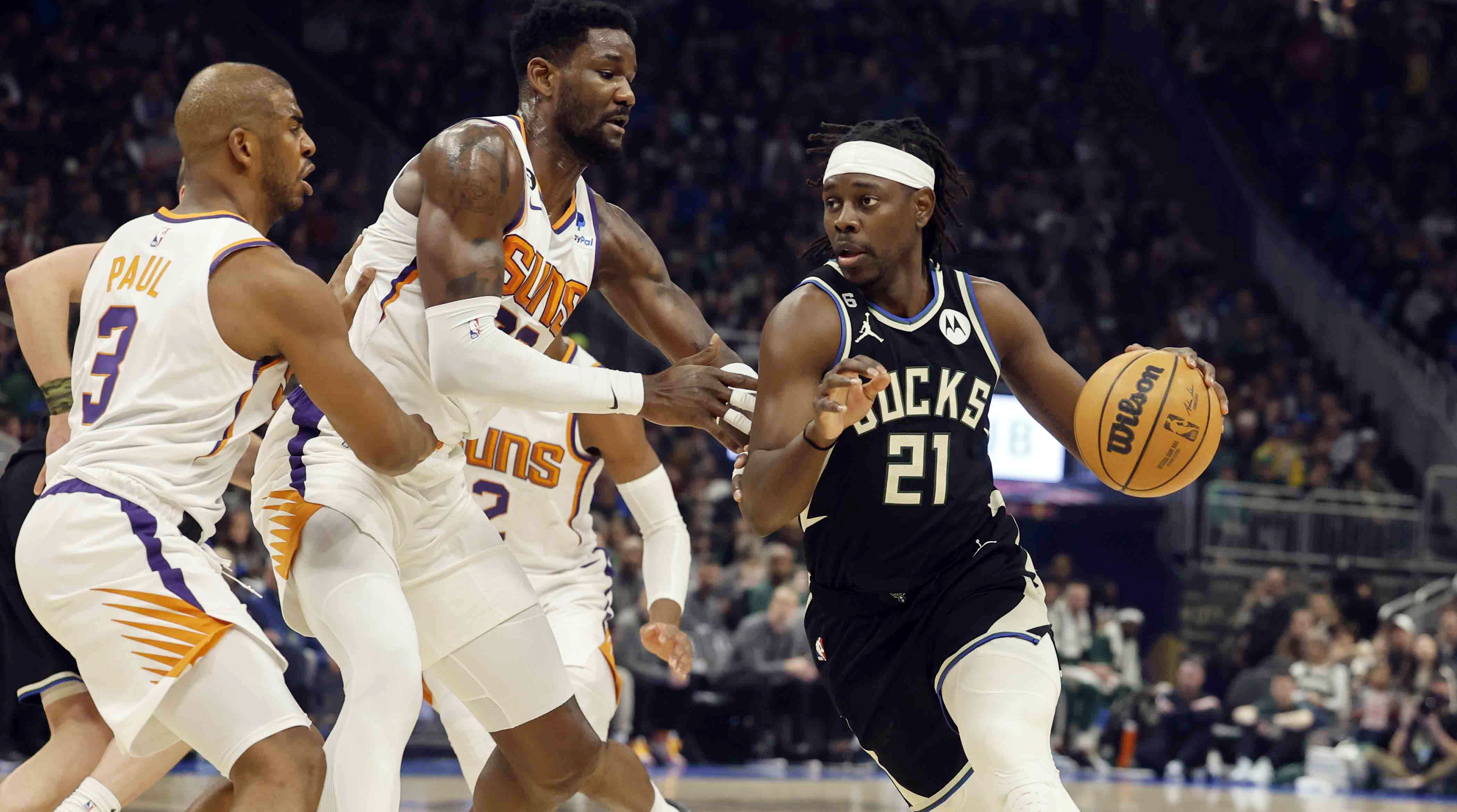 Bucks guard Jrue Holiday tries to dribble past Suns players Chris Paul and Deandre Ayton.
