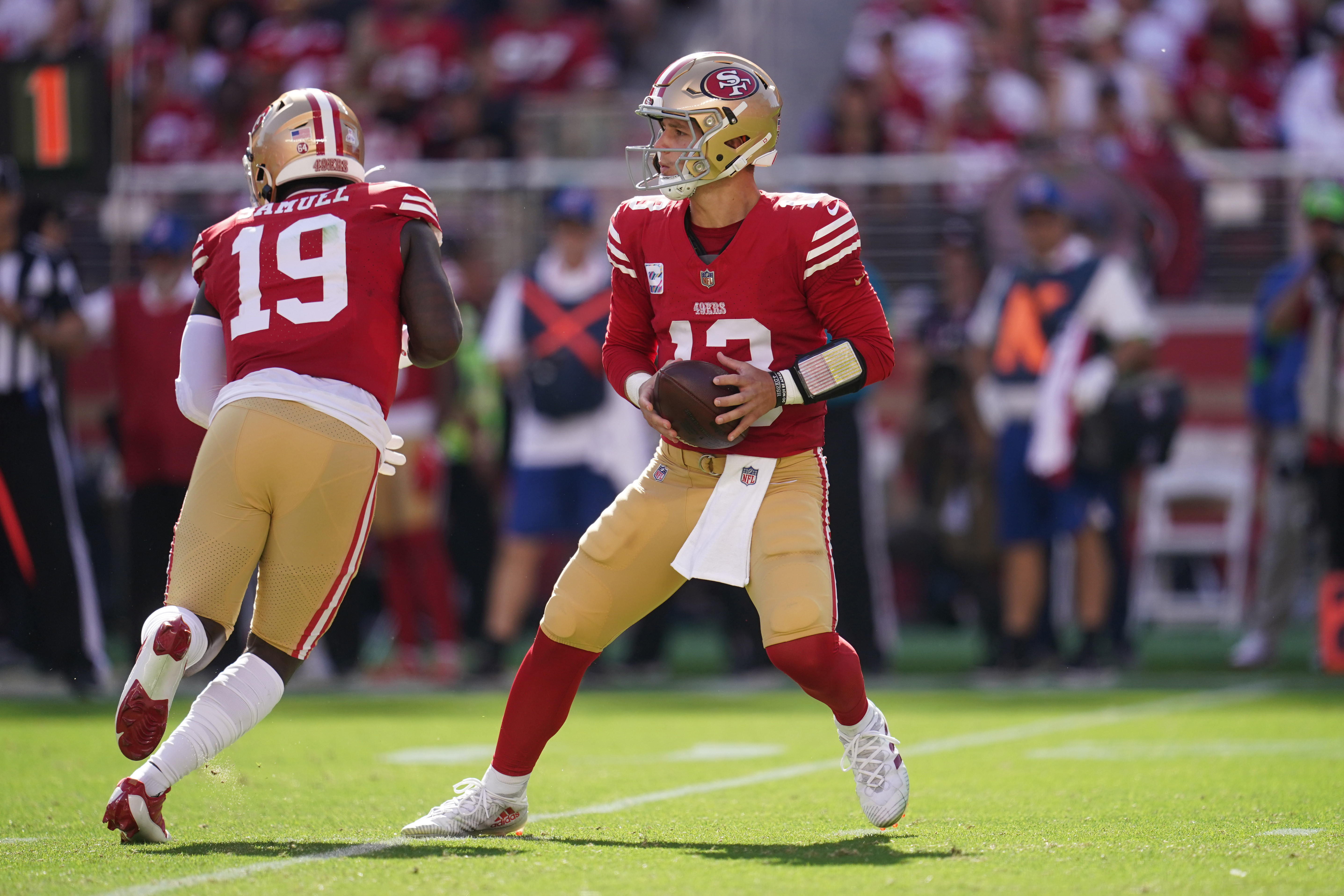 Brock Purdy holds the ball with two hands stepping back to throw