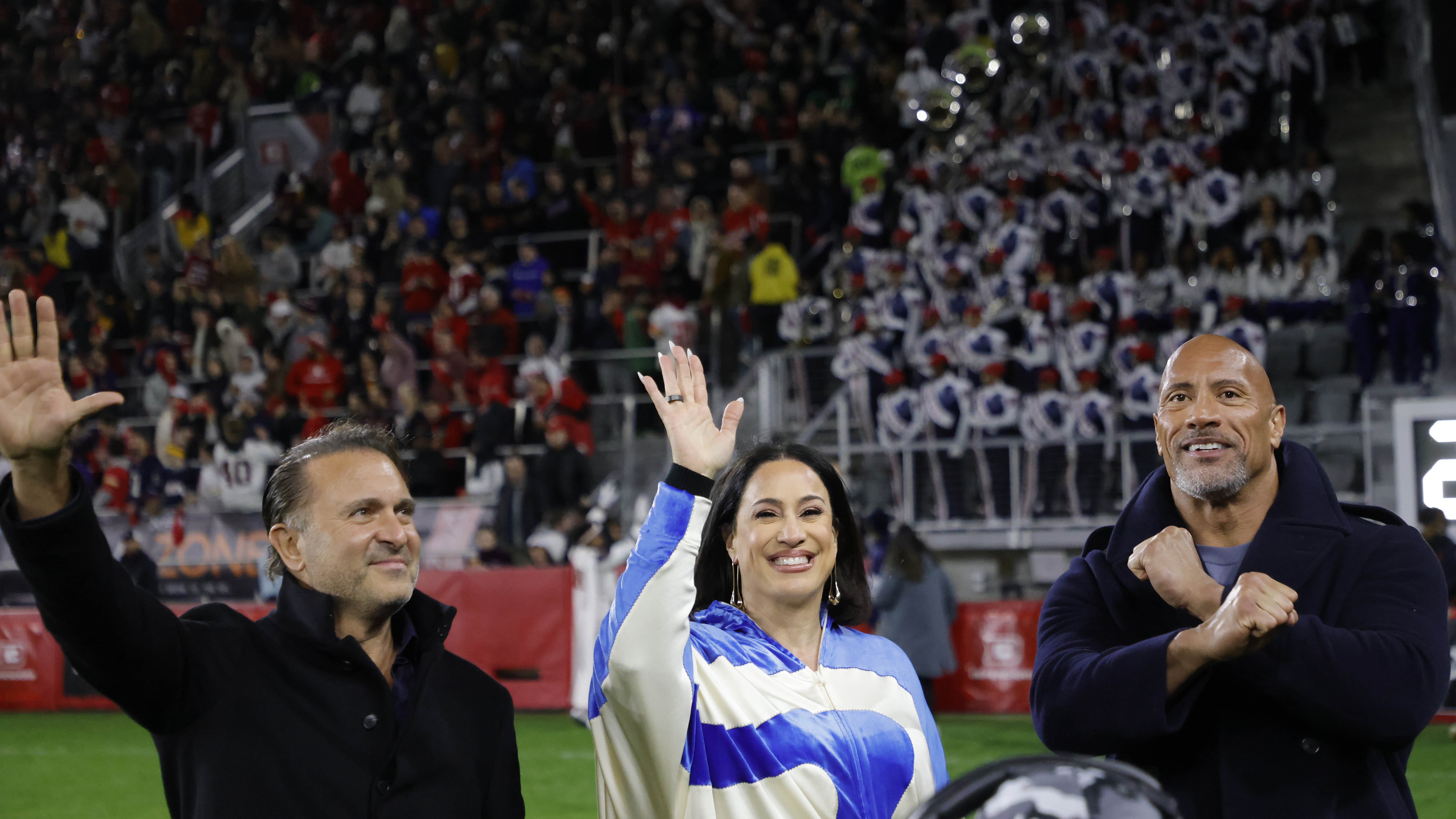 Feb 19, 2023; Washington, DC, USA; XFL co-owners Gerry Cardinale (L), Dany Garcia (M), and Dwayne Johnson (R) gestures to fans from the sideline during the game between the D.C. Defenders and the Seattle Sea Dragons in the second quarter at Audi Field. Mandatory Credit: Geoff Burke-USA TODAY Sports